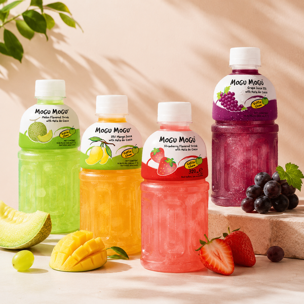 Four bottles of Mogu Mogu juice with fruit and grapes on a light background.